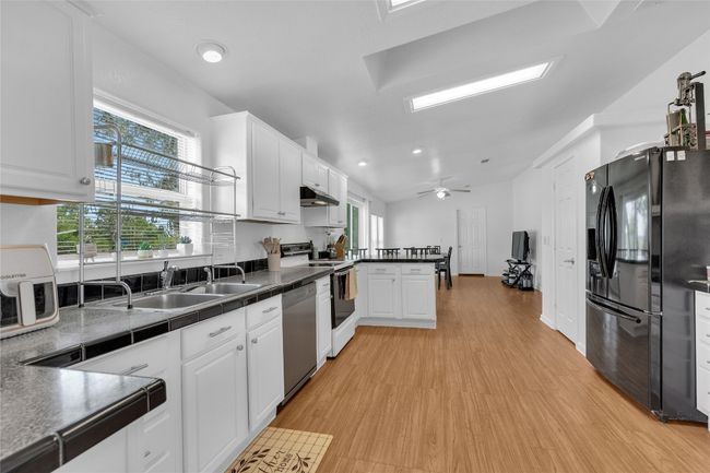 Kitchen with black fridge, white range with electric stovetop, under cabinet range hood, dishwasher, and white cabinetry | Image 10