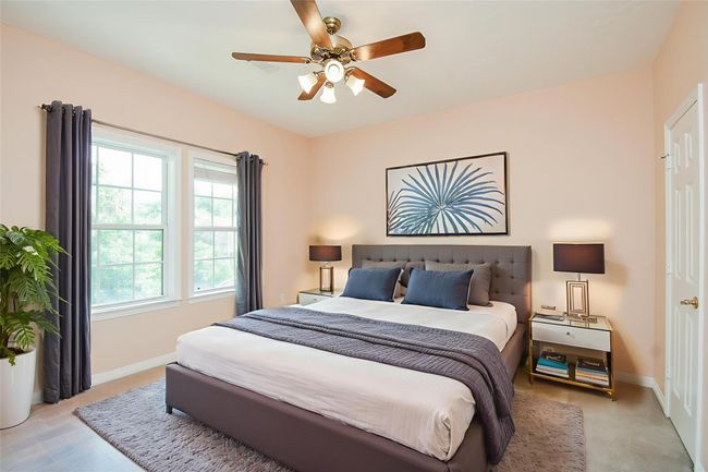 Bright bedroom with soft peach walls, two large windows offering natural light, a ceiling fan, and neutral carpeting. *Virtually staged | Image 40