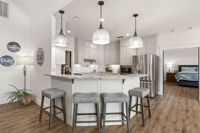 Kitchen with stainless steel appliances, a peninsula, crown molding, decorative backsplash, and a kitchen bar | Image 17