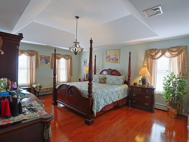 Bedroom featuring a tray ceiling, visible vents, a baseboard heating unit, and wood finished floors | Image 23