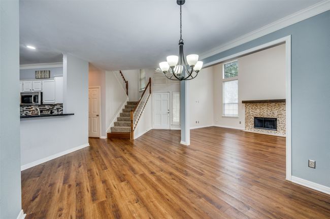 Unfurnished living room featuring crown molding, a chandelier, stairs, wood finished floors, and a tile fireplace | Image 5