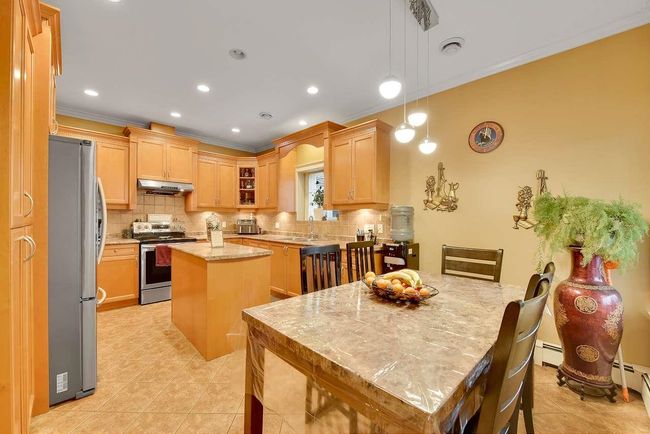 Kitchen featuring stainless steel appliances, under cabinet range hood, ornamental molding, a kitchen island, and backsplash | Image 27