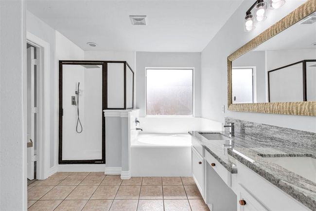 This bathroom features a spacious design with a tiled floor, a glass-enclosed shower, a large soaking tub, and a dual-sink vanity with granite countertops. Ample natural light enters through the window, creating a bright and inviting atmosphere. | Image 31