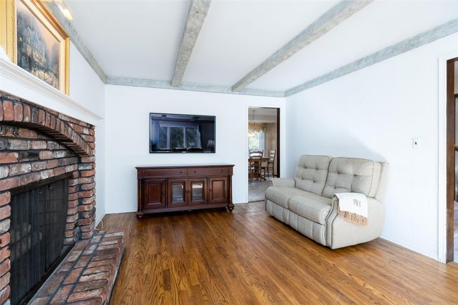 Living area featuring beam ceiling, wood finished floors, and a brick fireplace | Image 8