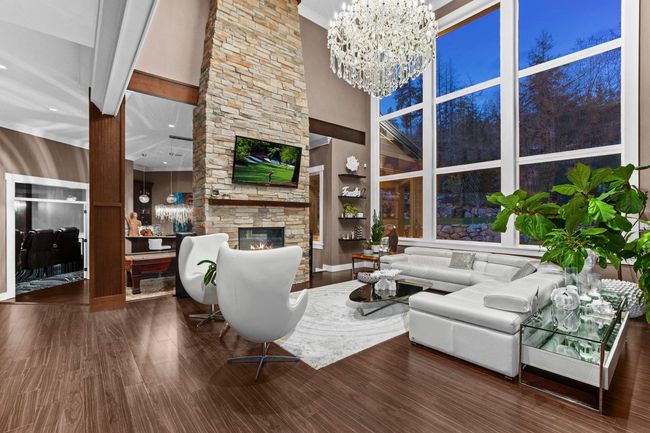 Living room featuring a high ceiling, wood finished floors, a chandelier, and a stone fireplace | Image 7