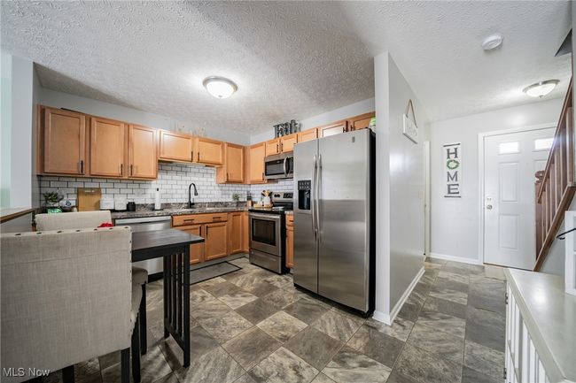 Kitchen with appliances with stainless steel finishes, dark tile patterned floors, a textured ceiling, and tasteful backsplash | Image 6