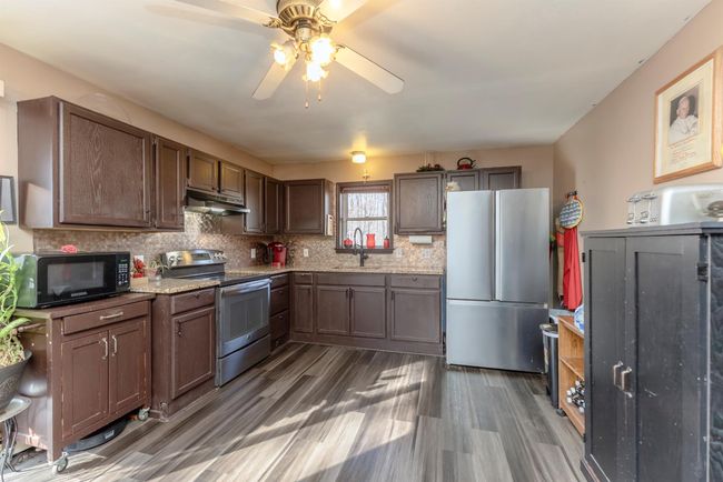 Kitchen with under cabinet range hood, ceiling fan, stainless steel appliances, a sink, and wood finished floors | Image 11