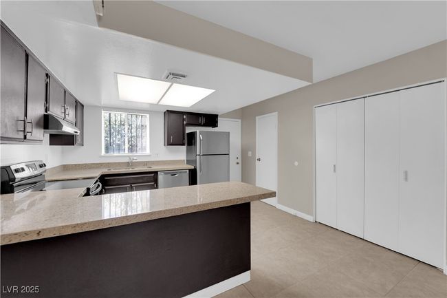 Kitchen with appliances with stainless steel finishes, under cabinet range hood, a peninsula, a sink, and light stone countertops | Image 11