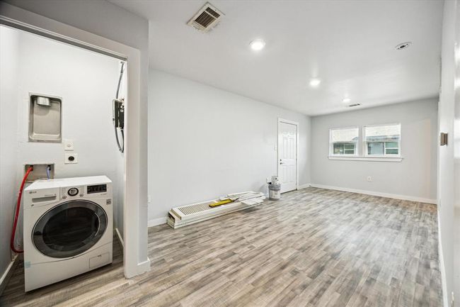 Bright and spacious utility or laundry room with modern wood-look flooring, recessed lighting, and a large window for natural light. The room includes a washer/dryer setup and ample space for additional storage or furnishings. | Image 9