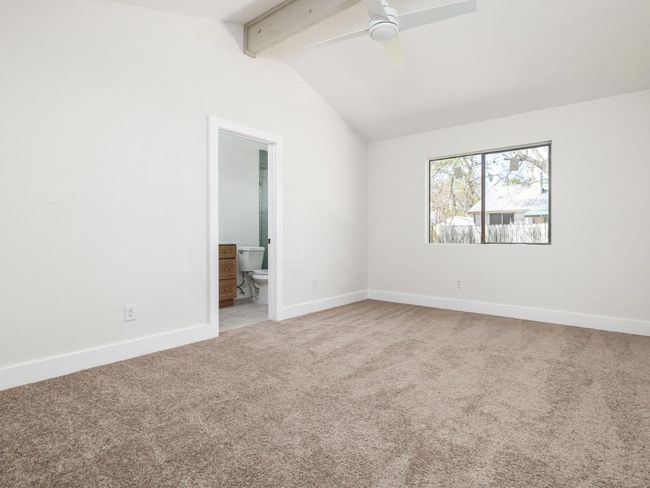 Carpeted empty room featuring baseboards, lofted ceiling with beams, and a ceiling fan | Image 22