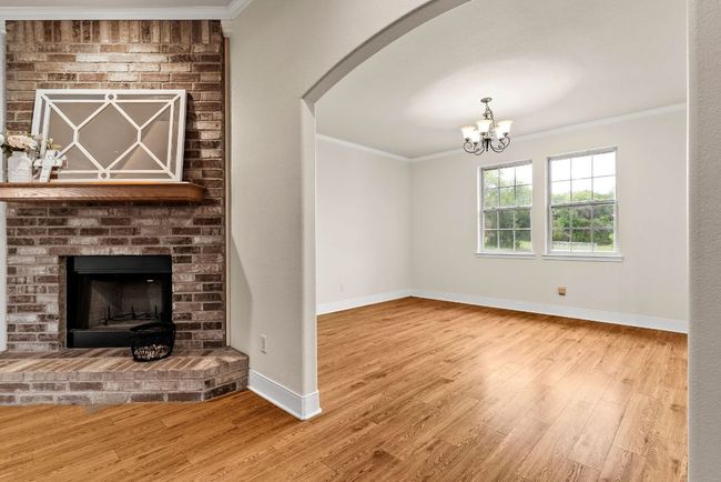 Unfurnished living room featuring baseboards, arched walkways, a brick fireplace, ornamental molding, and wood finished floors | Image 19