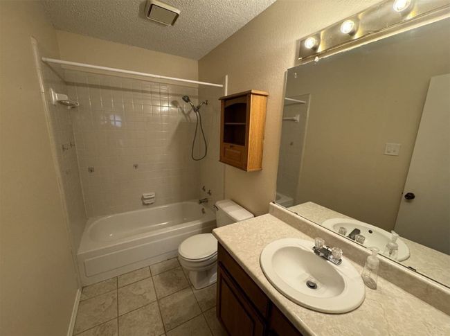Full bathroom with tiled shower / bath, tile flooring, oversized vanity, toilet, and a textured ceiling | Image 23
