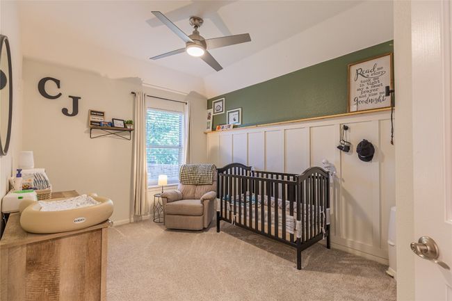 Carpeted bedroom with a crib, wainscoting, a ceiling fan, a decorative wall, and vaulted ceiling | Image 21