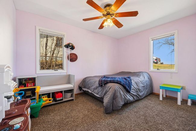 The second main-floor bedroom offers a cozy and inviting space, featuring soft carpeted flooring, a ceiling fan for added comfort, two windows that fill the room with natural light, and a spacious double closet for ample storage. | Image 9