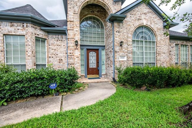 Charming brick home with a welcoming arched entryway and large windows. The well-maintained front yard features lush greenery and a curved walkway leading to the front door, creating an inviting first impression. | Image 6