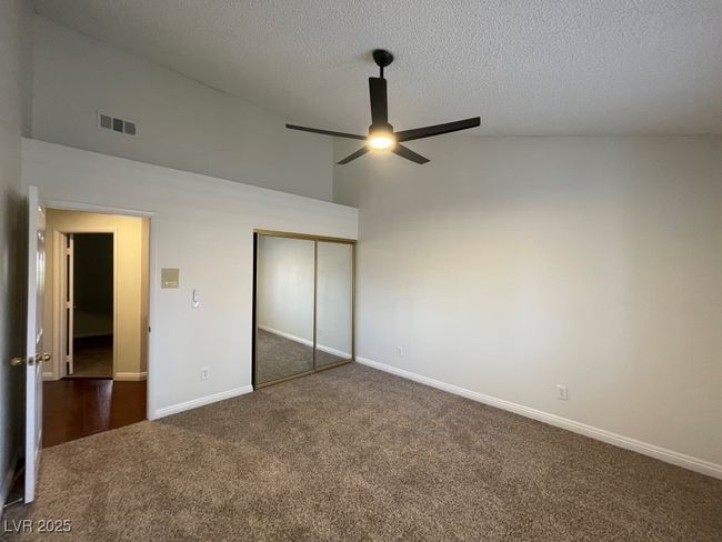 Unfurnished bedroom with dark carpet, high vaulted ceiling, a closet, a textured ceiling, and ceiling fan | Image 23