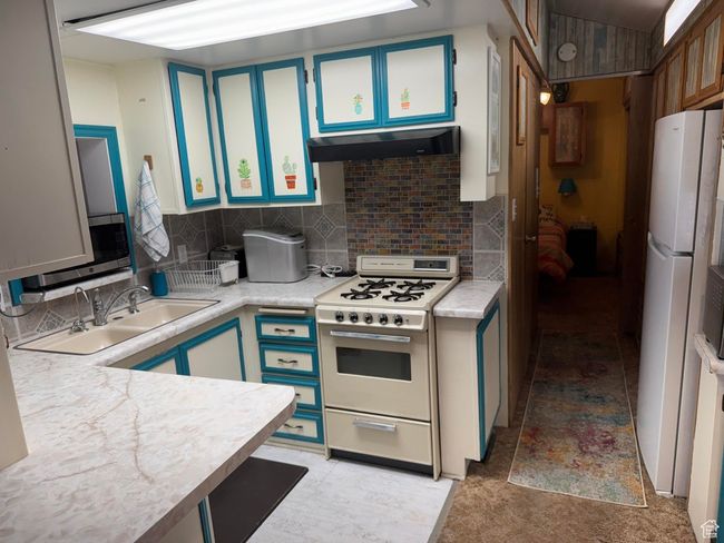 Kitchen with gas range oven, freestanding refrigerator, light countertops, backsplash, and stainless steel microwave | Image 9