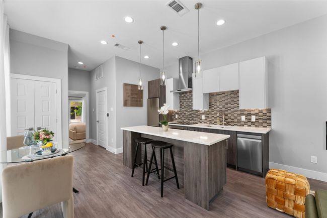 Kitchen featuring wall chimney exhaust hood, stainless steel appliances, baseboards, a kitchen bar, and visible vents | Image 6