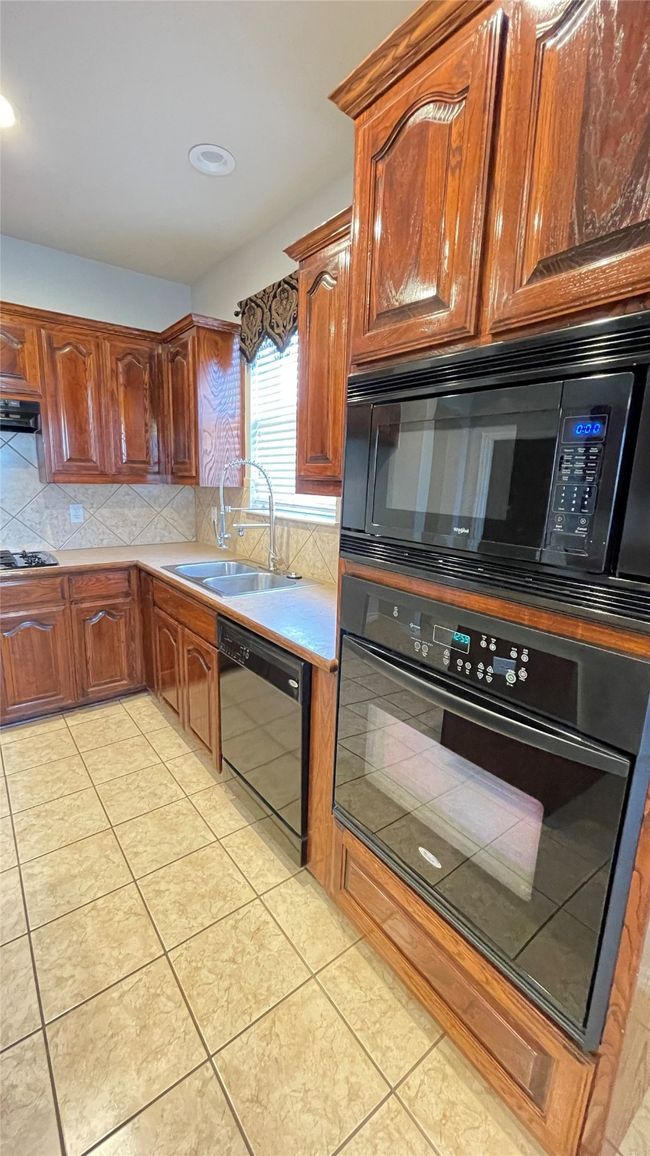 Kitchen with black appliances, decorative backsplash, light tile patterned floors, light countertops, and range hood | Image 8