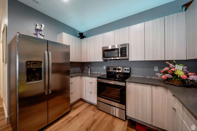 Kitchen featuring appliances with stainless steel finishes, light wood-type flooring, dark countertops, and modern cabinets | Image 5