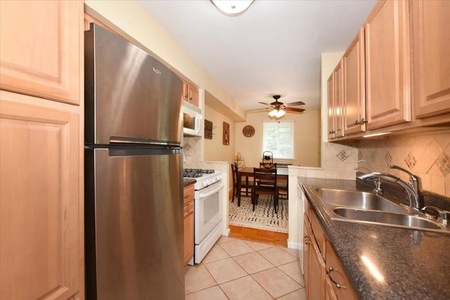 Kitchen with white appliances, decorative backsplash, light tile patterned floors, a ceiling fan, and light brown cabinets | Image 18