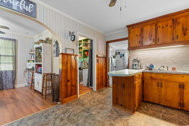 Kitchen with a ceiling fan, wallpapered walls, ornamental molding, light countertops, and brown cabinetry | Image 18