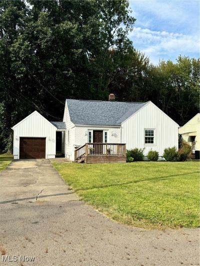 Modern farmhouse featuring a wooden deck, a garage, a front lawn, and an outbuilding | Image 1