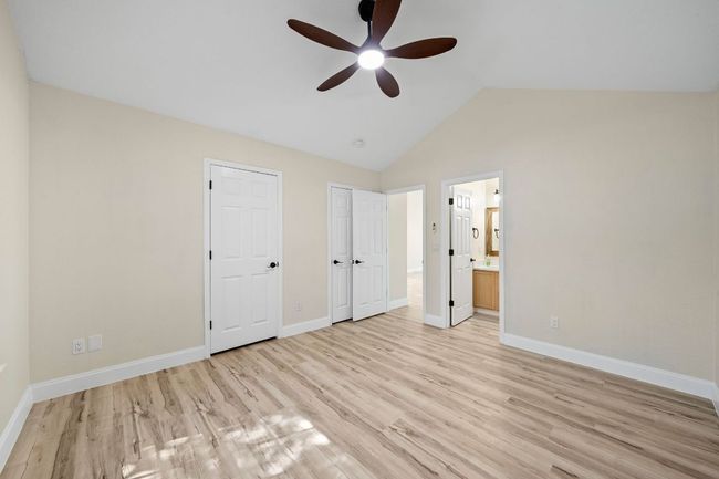 Unfurnished bedroom featuring light wood-type flooring, connected bathroom, lofted ceiling, and ceiling fan | Image 29
