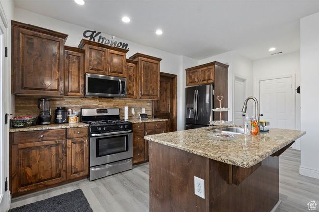 Kitchen featuring stainless steel appliances, sink, a kitchen breakfast bar, a kitchen island with sink, and decorative backsplash | Image 9