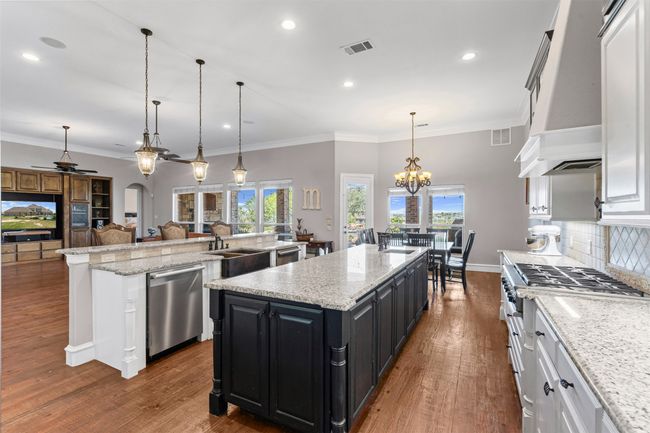 Kitchen featuring ceiling fan with notable chandelier, a large island, dishwasher, dark cabinetry, and custom range hood | Image 4