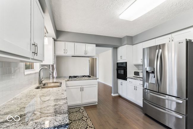 kitchen featuring dark wood finished floors, light stone countertops, white cabinets, appliances with stainless steel finishes, and a sink | Image 11
