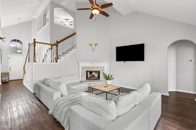 Living area with a ceiling fan, high vaulted ceiling, laminate flooring, arched walkways, and stairway | Image 18