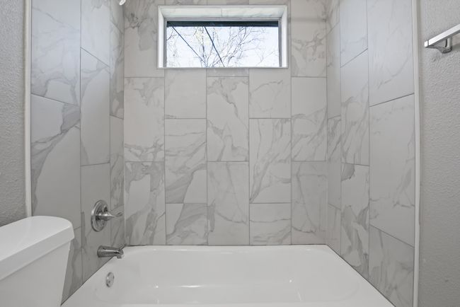 Bathroom with bathing tub / shower combination, toilet, and a textured wall | Image 14