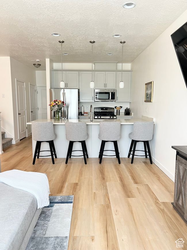 Kitchen with appliances with stainless steel finishes, a textured ceiling, a kitchen breakfast bar, light wood-style flooring, and light countertops | Image 6