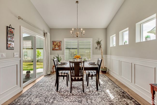 Dining room with light wood finished floors, vaulted ceiling, a decorative wall, wainscoting, and a notable chandelier | Image 13