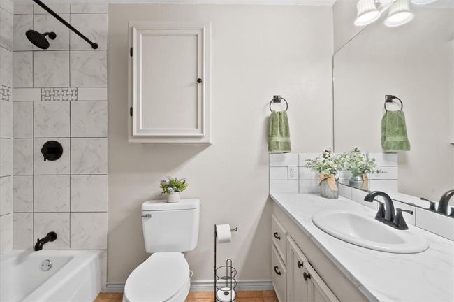 A charming full bath is easily accessible to both secondary bedrooms and the living space. It features a tub and shower combination, quartz counters, and classic lighting. | Image 16