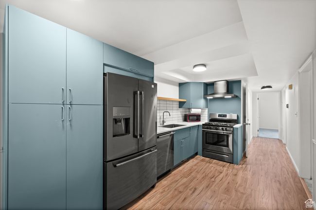Kitchen featuring stainless steel appliances, wall chimney range hood, a sink, open shelves, and light wood-style flooring | Image 7