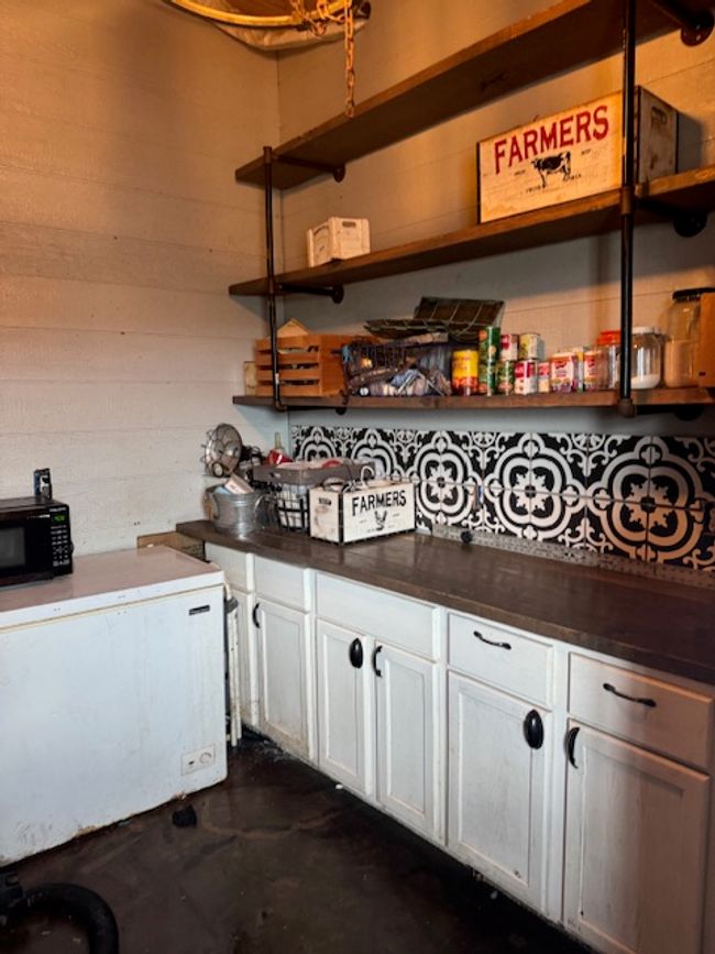 Kitchen with unfinished concrete floors, white cabinetry, fridge, and open shelves | Image 9