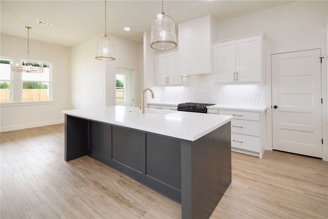 Kitchen with backsplash, a sink, a center island with sink, white cabinets, and light wood-style flooring | Image 10