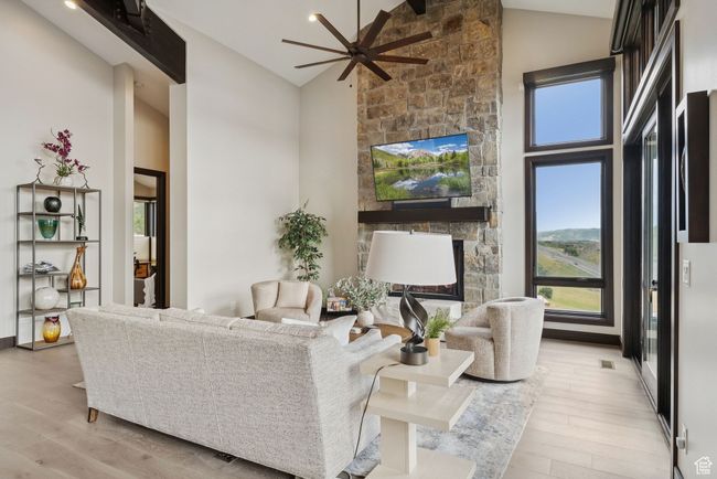 Living area with healthy amount of natural light, wood finished floors, high vaulted ceiling, a stone fireplace, and ceiling fan | Image 17