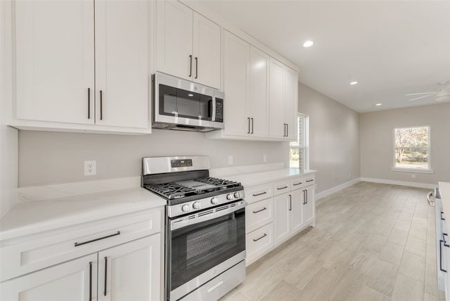 Kitchen with stainless steel appliances, white cabinetry, recessed lighting, ceiling fan, and light stone counters | Image 14
