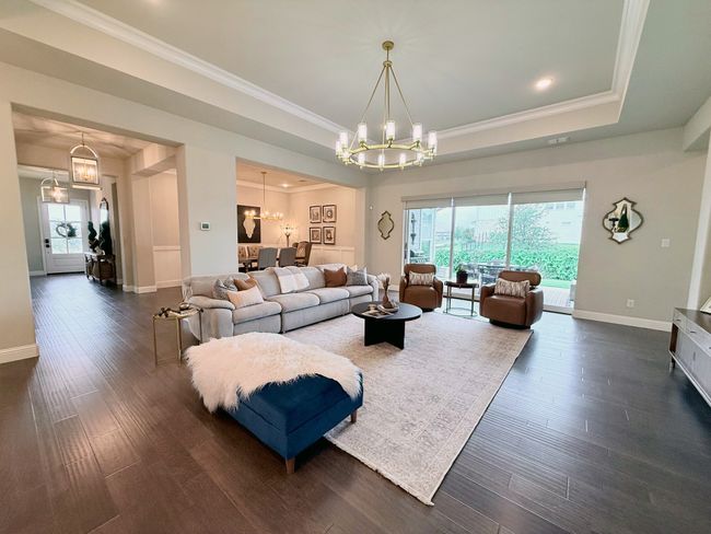 Living area featuring a raised ceiling, a chandelier, crown molding, dark wood-style flooring, and recessed lighting | Image 6