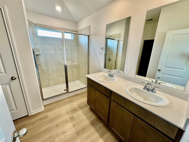Full bath featuring a stall shower, wood finished floors, double vanity, a textured wall, and lofted ceiling | Image 4