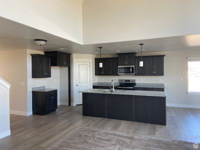 Kitchen featuring a kitchen island with sink, hanging light fixtures, stainless steel appliances, light stone counters, and light hardwood / wood-style floors | Image 3