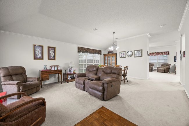 Carpeted living room with healthy amount of natural light, crown molding, a chandelier, and a textured ceiling | Image 7