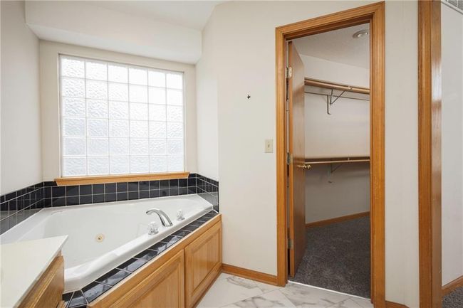 Full bath with a jetted tub, marble finish floors, a walk in closet, and baseboards | Image 21