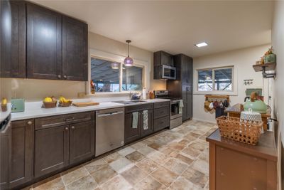 Kitchen featuring stainless steel appliances, dark brown cabinetry, decorative light fixtures, and plenty of natural light | Image 3