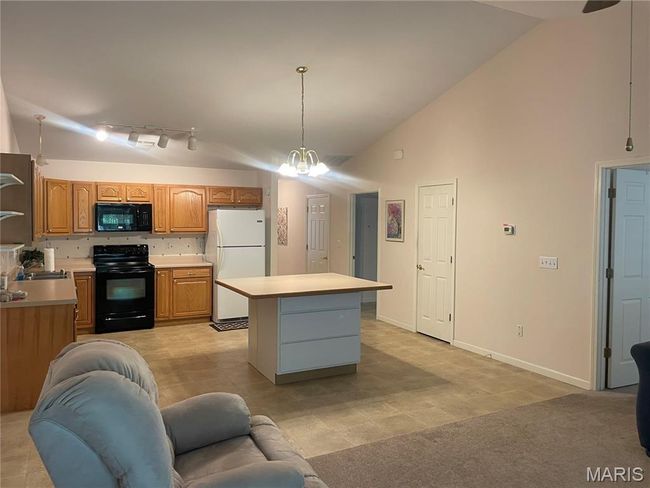 Kitchen with black appliances, light countertops, a center island, hanging light fixtures, and high vaulted ceiling | Image 10