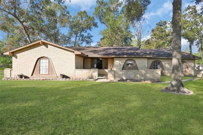 Charming single-story brick home with a spacious front lawn and mature trees, featuring distinctive arched windows and a cozy covered entrance. | Image 1