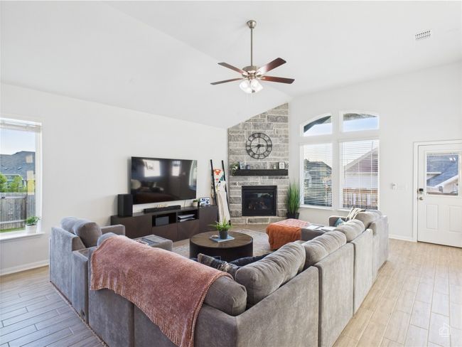 Living room with light wood finished floors, ceiling fan, a fireplace, baseboards, and high vaulted ceiling | Image 15
